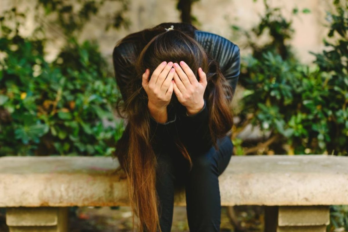 Woman covering her face with her head down and elbows on her knees, indicating traumatic experience but also a sense of hope through giving herself a break representing the title of the blog: Overcoming Vicarious Trauma & Discovering Self-compassion