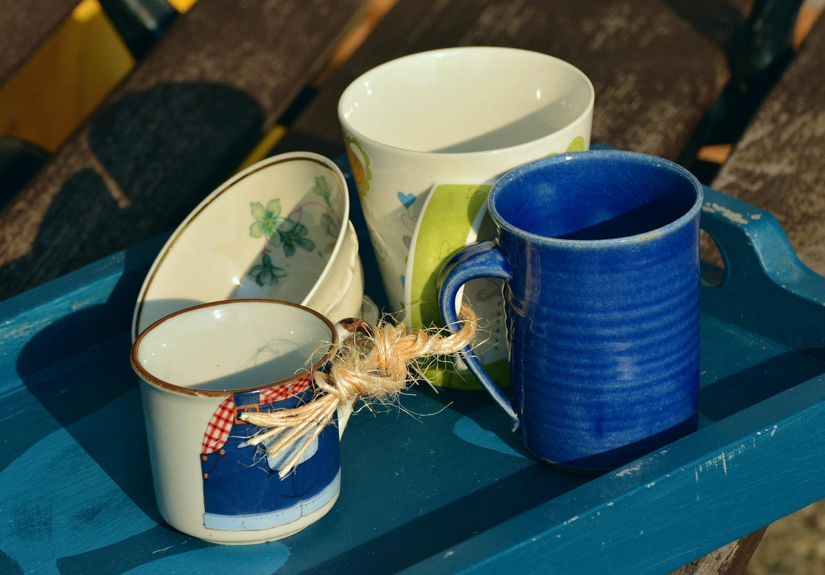 Four teacups, connected by a natural string, sit on a wooden tray.